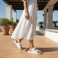 Person wearing white pants and sandals on a tiled patio with plants and a clear sky in the background