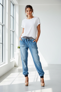 Woman wearing a white t-shirt and blue jeans standing in a bright room with large windows.