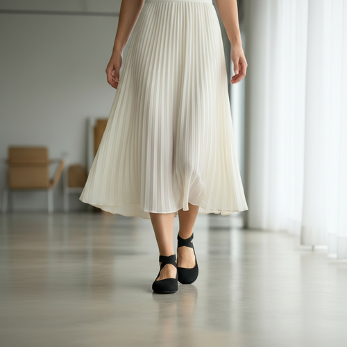 Person wearing a white pleated skirt and black shoes in an indoor setting