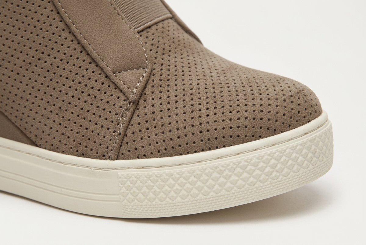 Close-up of a slip-on sneaker in taupe brown with perforated upper panels and a thick cream-colored sole.