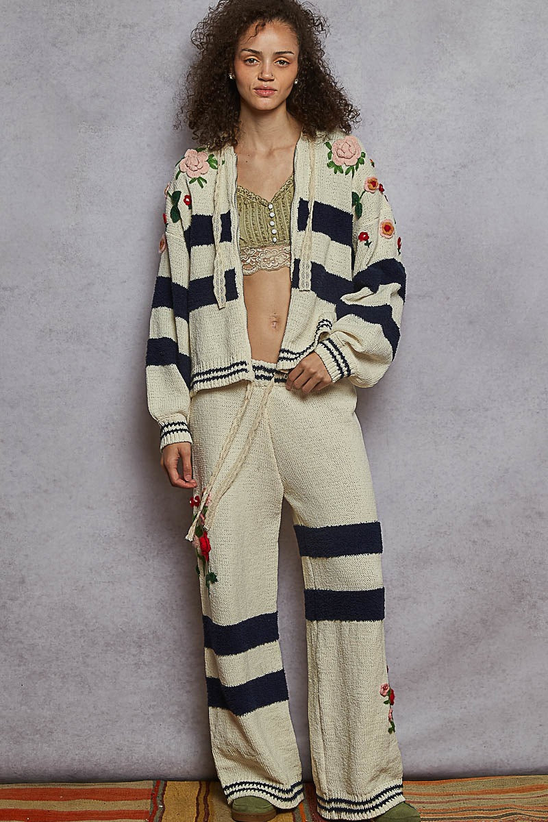 Woman wearing a floral embroidered cardigan and matching pants against a gray background