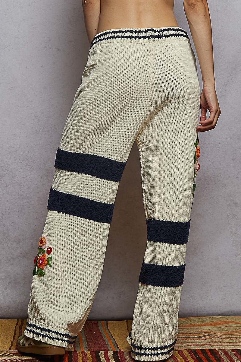 Beige pants with black stripes and floral embroidery on a neutral background