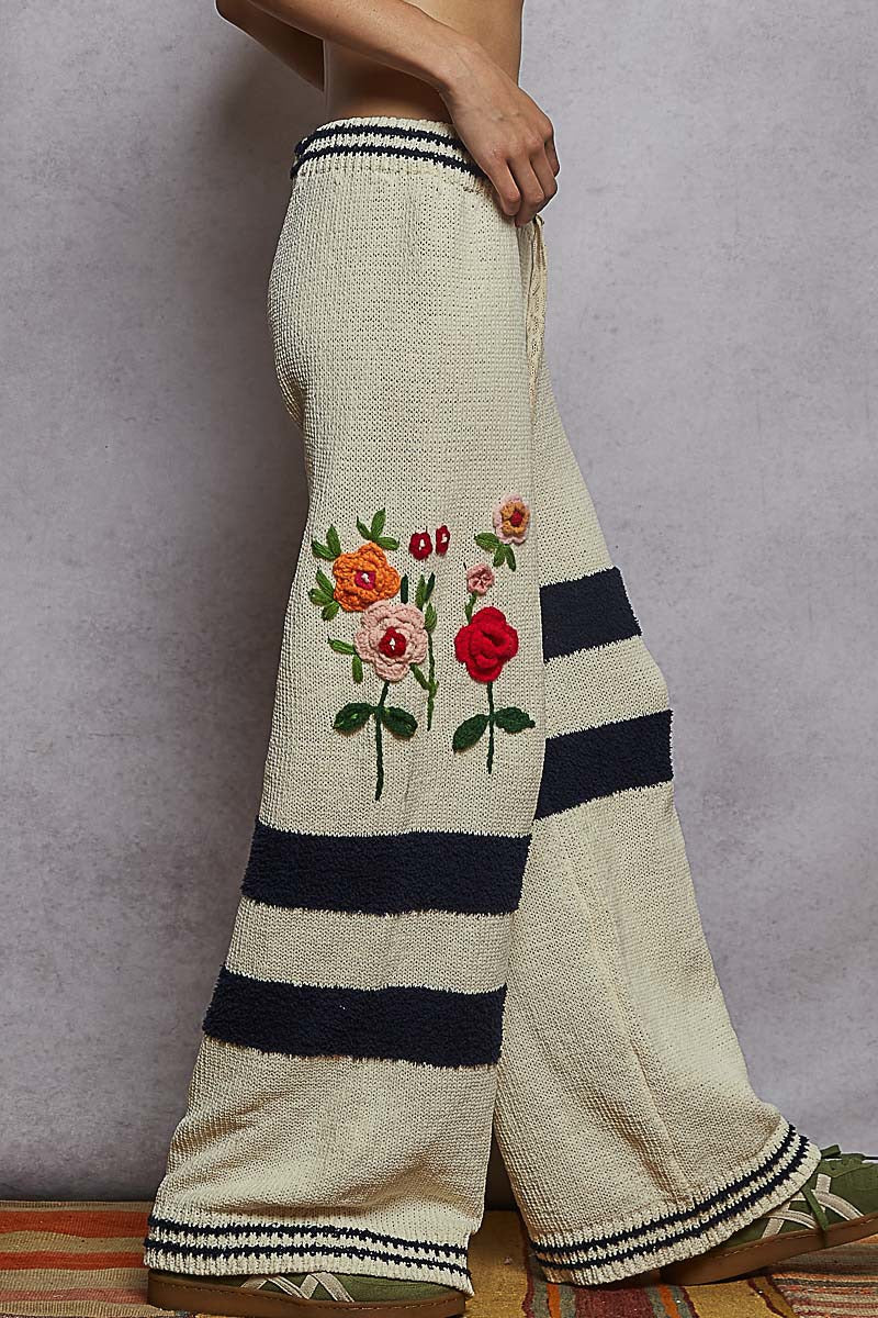 Beige pants with floral embroidery and black stripes on a plain background