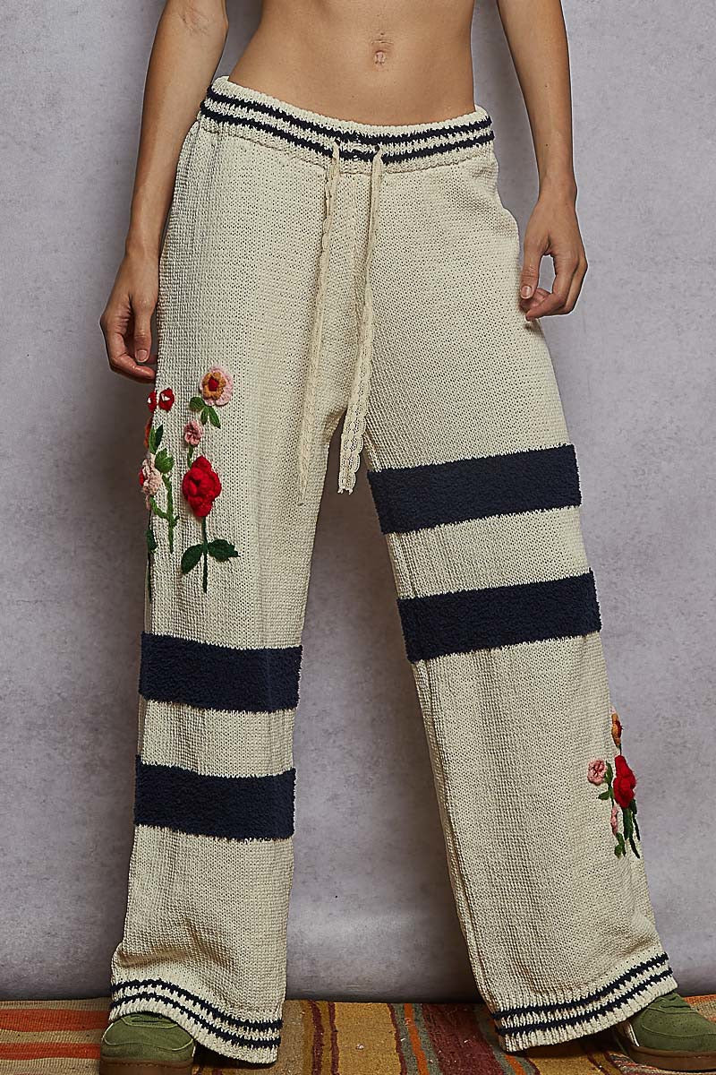 Knitted pants with floral embroidery and black stripes on a plain background