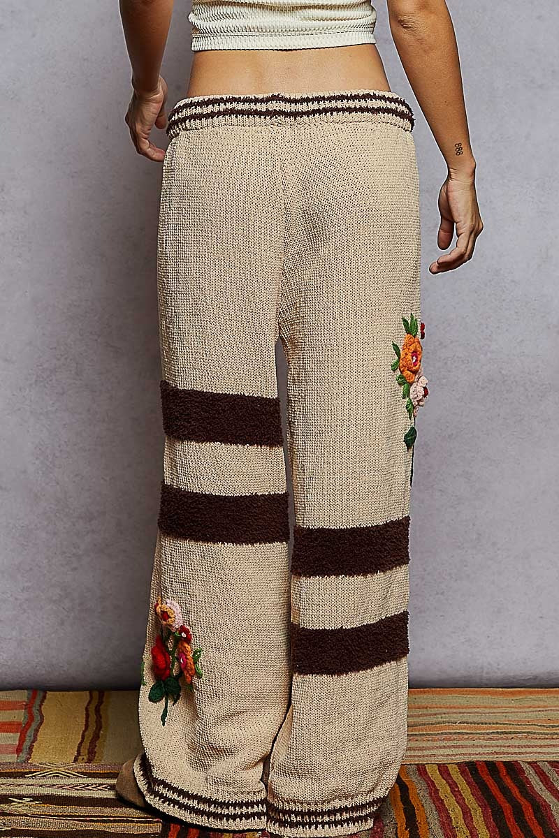 Beige knitted pants with brown stripes and floral embroidery on a gray background