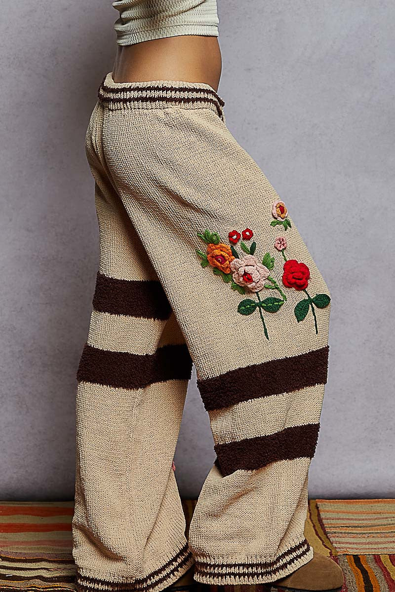 Beige knitted pants with floral embroidery and brown stripes on a neutral background