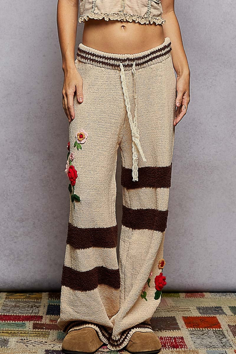 Beige and brown striped pants with floral embroidery on a plain background
