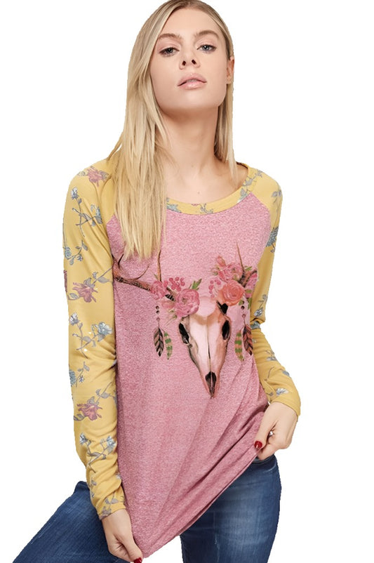 A blonde woman with long hair models a cotton t-shirt with floral print sleeves, a deer skull graphic on the front, and blue jeans.