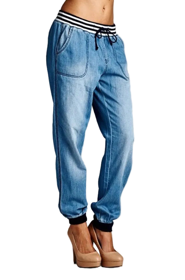 Blue denim jogger pants with a striped waistband on a white background